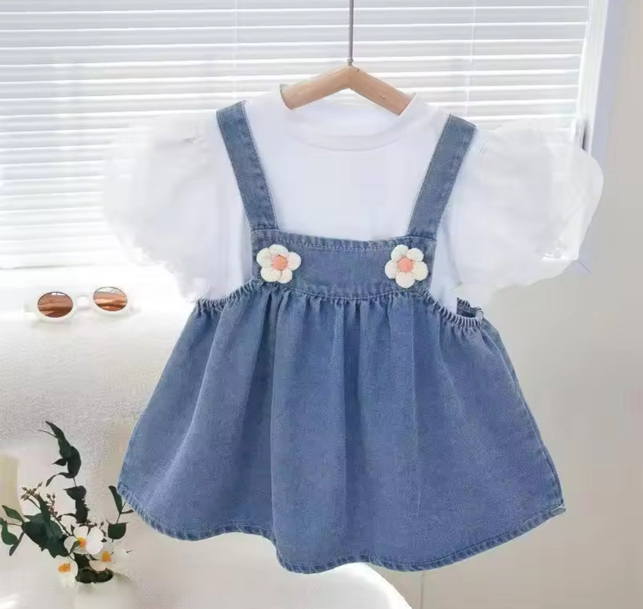 Children's outfit with a white shirt and blue denim dress with floral details on a wooden hanger.