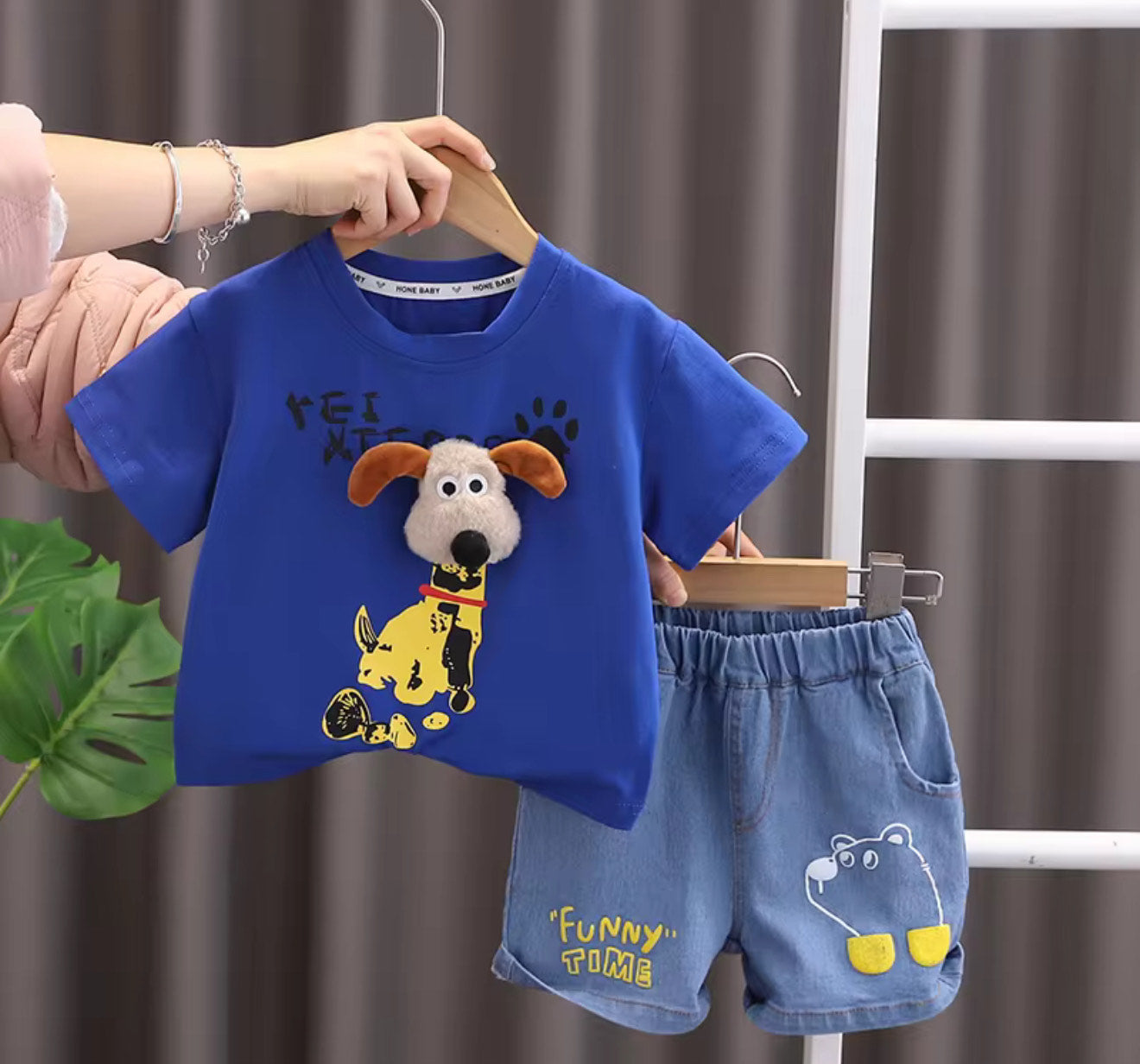 A set of children's clothing, featuring a blue t-shirt with a cartoon character and soft denim shorts, displayed on a hanger.